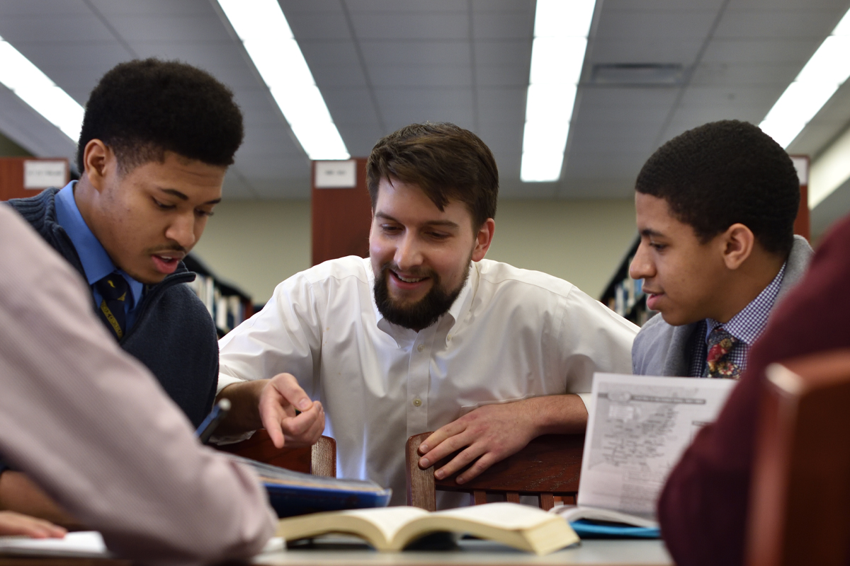 Mentor sits with two students in the library